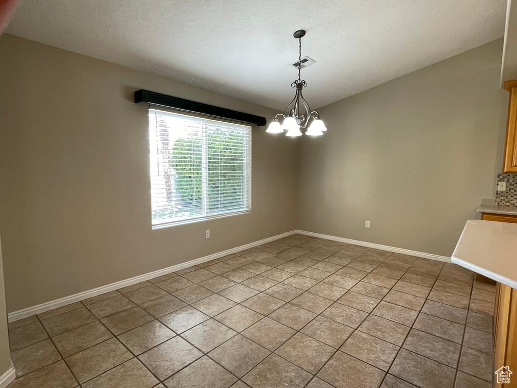 Spare room with light tile patterned floors, visible vents, a chandelier, and baseboards