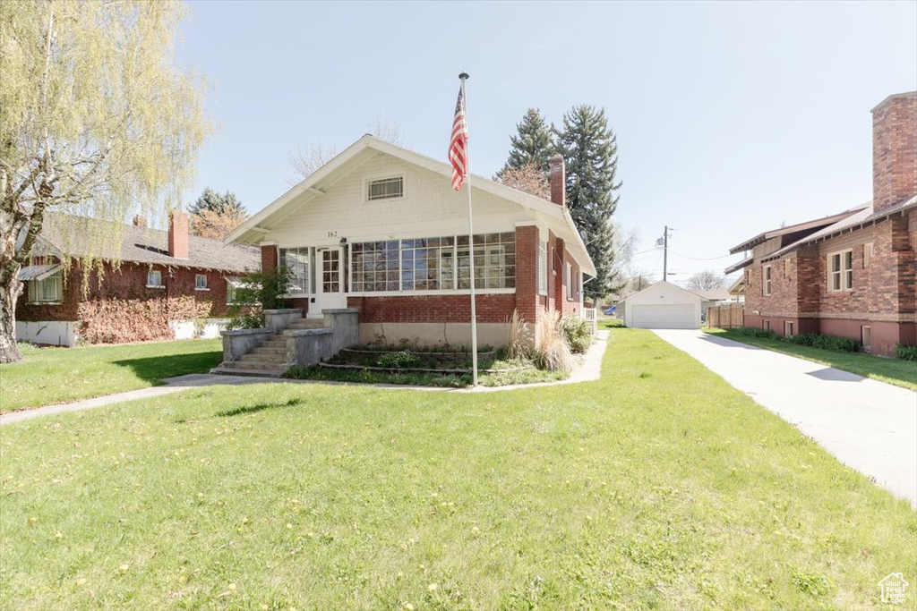 Bungalow-style home with a detached garage, an outdoor structure, a front lawn, and brick siding