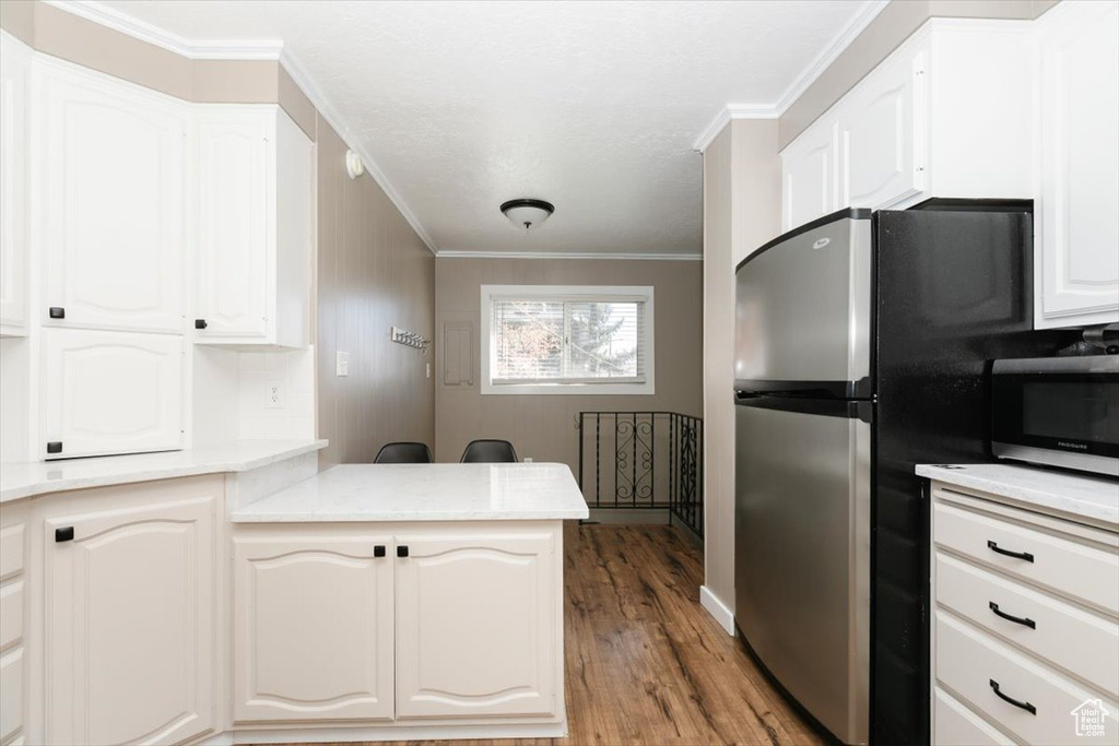 Kitchen featuring white cabinets, appliances with stainless steel finishes, a peninsula, wood finished floors, and ornamental molding