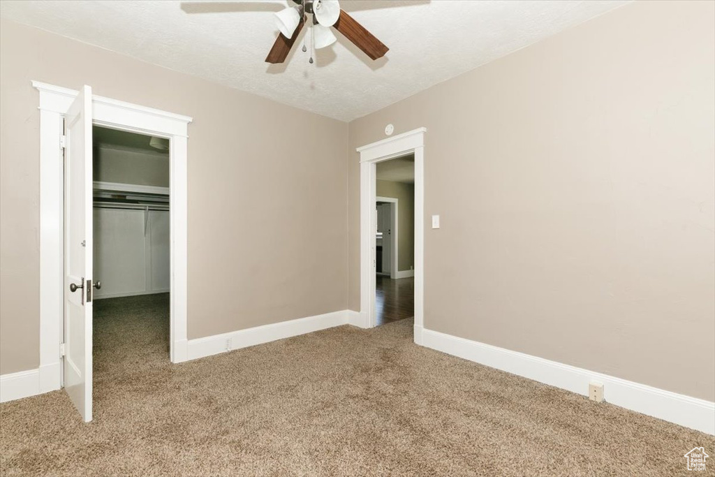 Unfurnished bedroom featuring a walk in closet, carpet floors, a ceiling fan, baseboards, and a closet