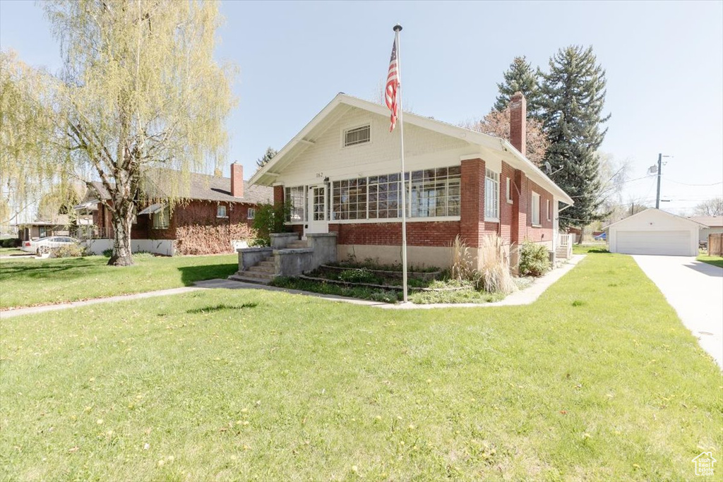 Bungalow featuring a chimney, an outbuilding, a garage, brick siding, and a front lawn