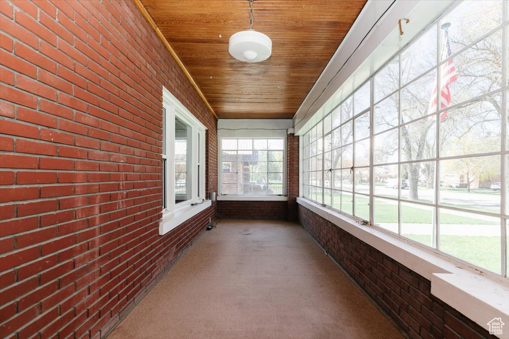 Unfurnished sunroom with wooden ceiling, carpet flooring, and brick wall
