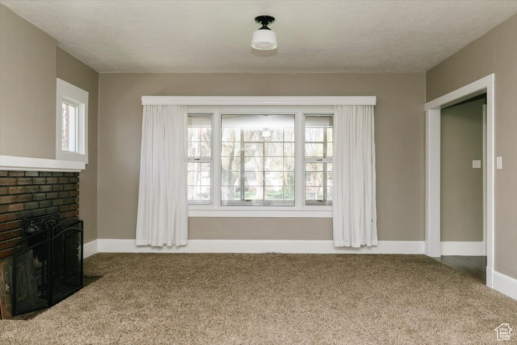 Unfurnished living room featuring baseboards, carpet flooring, a textured ceiling, and a brick fireplace