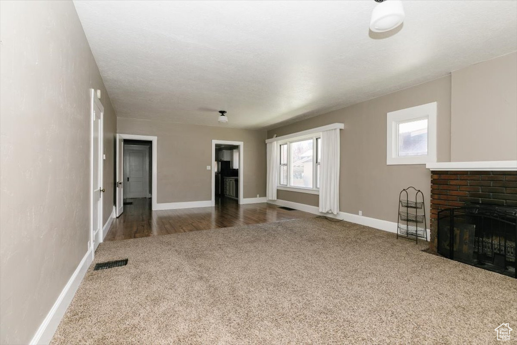 Unfurnished living room featuring carpet floors, baseboards, visible vents, and a fireplace