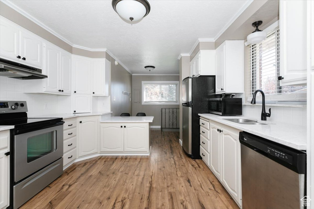 Kitchen featuring a sink, under cabinet range hood, white cabinets, and stainless steel appliances