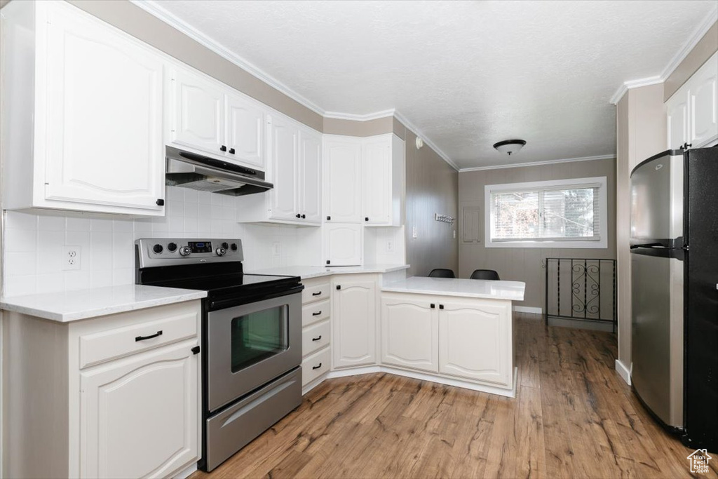 Kitchen featuring appliances with stainless steel finishes, light countertops, a peninsula, under cabinet range hood, and light wood-style flooring