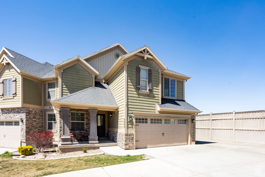 Craftsman house with covered porch, fence, driveway, stone siding, and an attached garage
