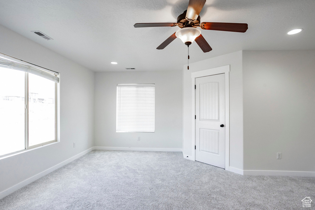 Unfurnished room featuring a ceiling fan, visible vents, light carpet, and plenty of natural light