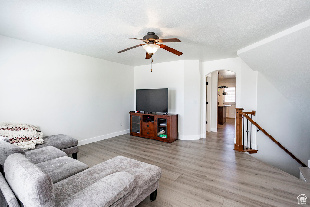 Living room featuring light wood finished floors, arched walkways, ceiling fan, and baseboards