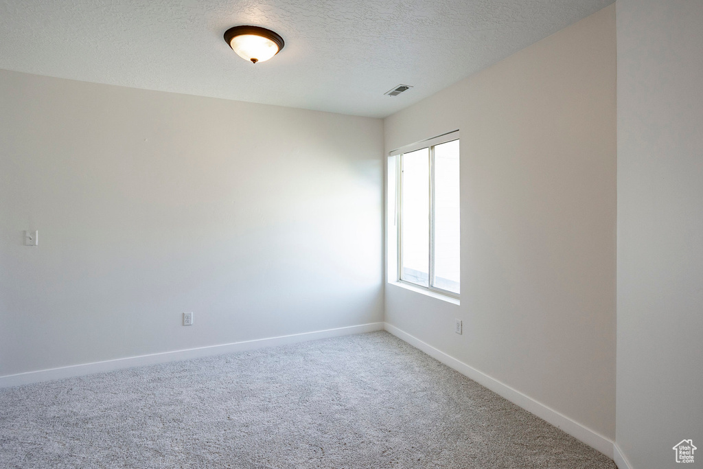 Spare room featuring a textured ceiling, visible vents, baseboards, and carpet floors