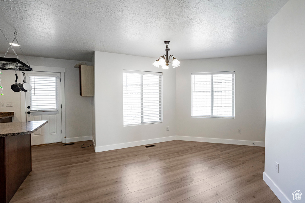 Unfurnished dining area featuring a textured ceiling, a chandelier, wood finished floors, and visible vents