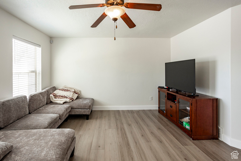 Living area featuring a textured ceiling, ceiling fan, light wood-type flooring, and baseboards