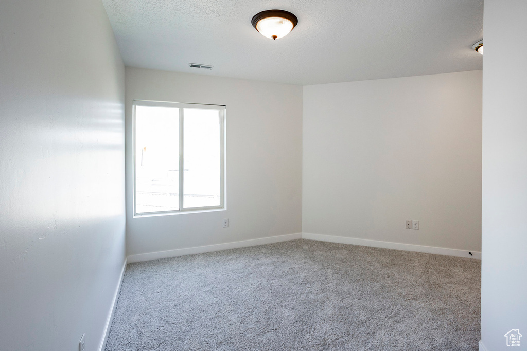 Unfurnished room featuring carpet flooring, a textured ceiling, visible vents, and baseboards