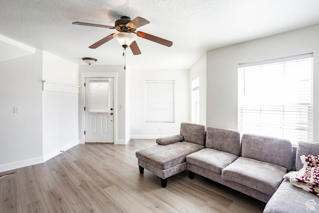 Living room featuring baseboards, a ceiling fan, a textured ceiling, and light wood-style flooring