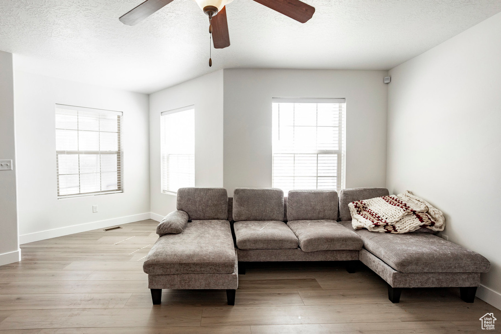 Living room featuring light wood-style floors, baseboards, visible vents, a ceiling fan, and a textured ceiling