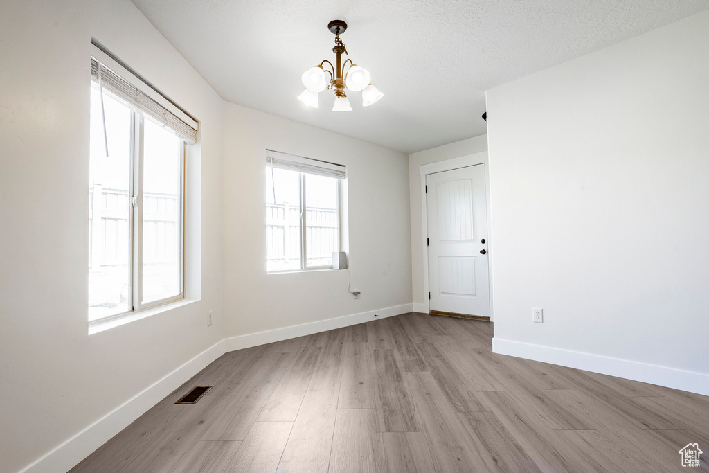 Unfurnished room featuring light wood finished floors, visible vents, a chandelier, and baseboards