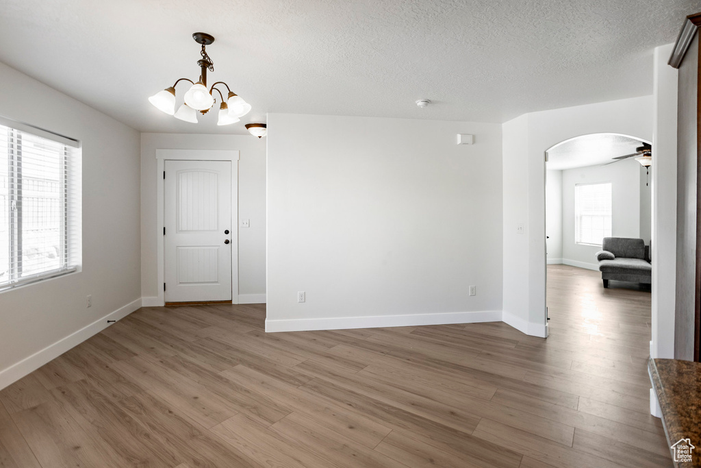 Spare room featuring baseboards, arched walkways, a notable chandelier, and light wood-style floors