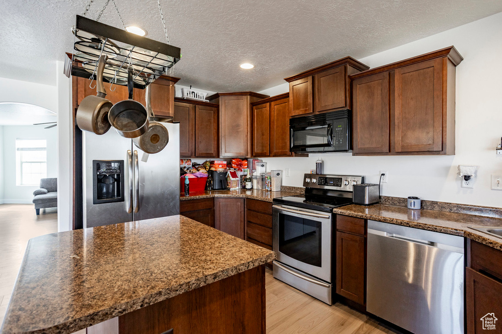 Kitchen with a textured ceiling, appliances with stainless steel finishes, dark countertops, arched walkways, and light wood finished floors