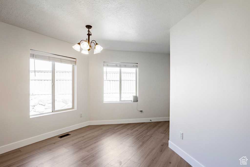 Spare room with a chandelier, visible vents, a wealth of natural light, and light wood-style flooring