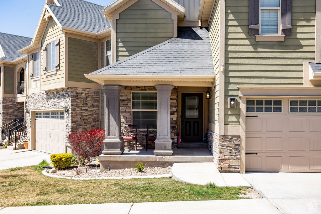 Craftsman house with a porch, a shingled roof, a garage, driveway, and stone siding
