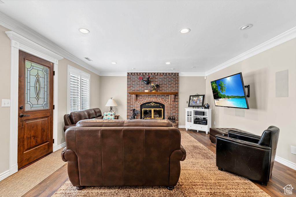 Living room with ornamental molding, a brick fireplace, wood finished floors, and recessed lighting
