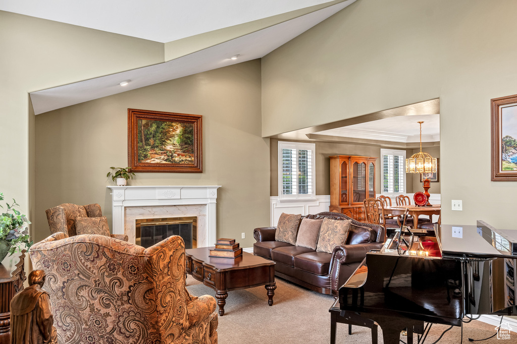Living area with high vaulted ceiling, light carpet, an inviting chandelier, a premium fireplace, and ornamental molding