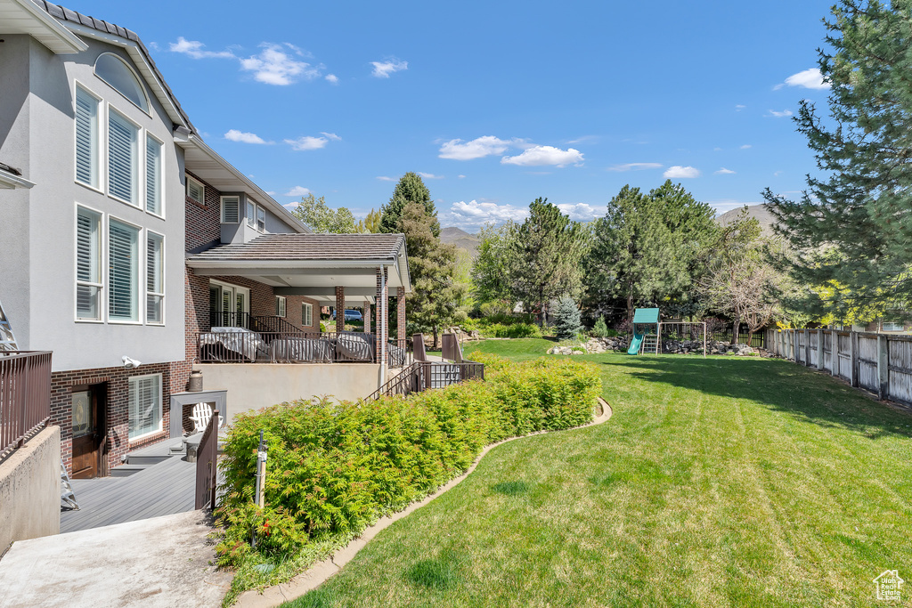 View of yard featuring fence, a deck with mountain view, and a playground