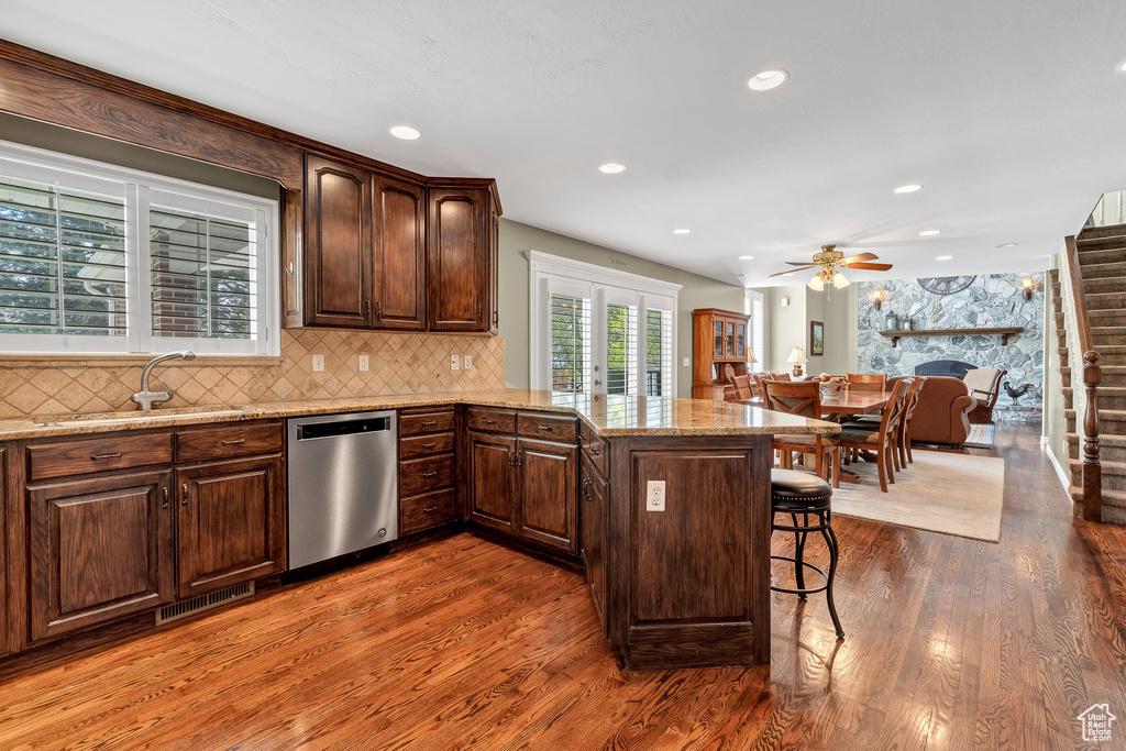 Kitchen featuring stainless steel dishwasher, a kitchen breakfast bar, a sink, and dark wood-type flooring