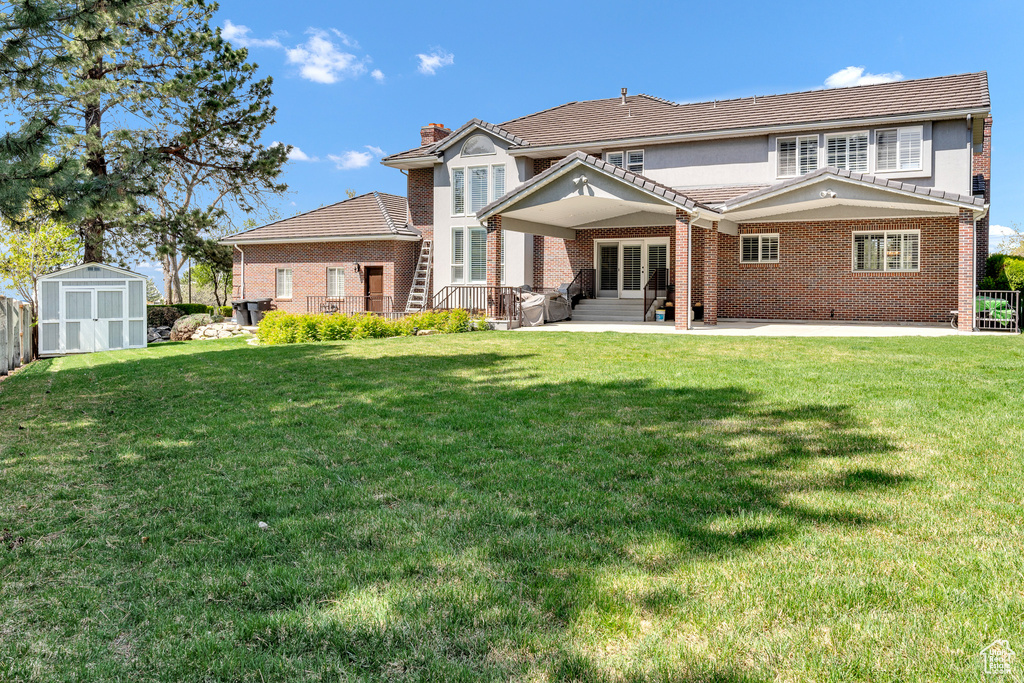 Rear view of house featuring brick siding, a lawn, an outbuilding, and a storage shed