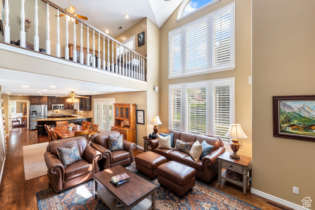 Living room with high vaulted ceiling, a ceiling fan, baseboards, dark wood-type flooring, and visible vents