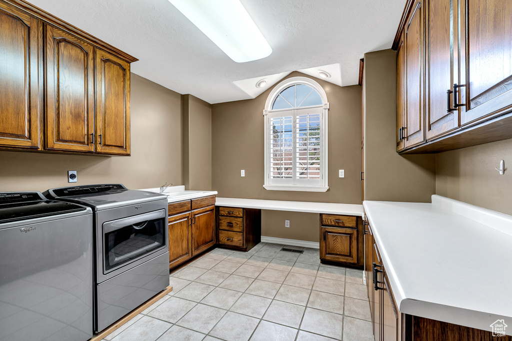 Clothes washing area featuring washing machine and clothes dryer, a sink, light tile patterned floors, cabinet space, and visible vents