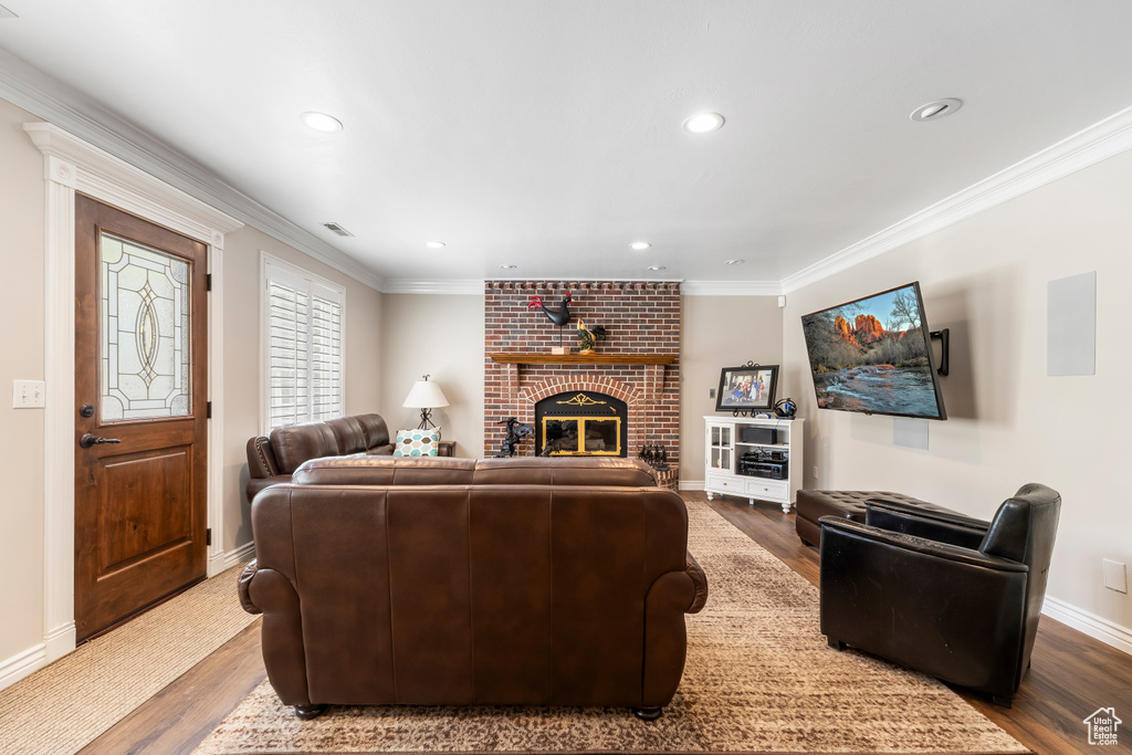 Living area with recessed lighting, wood finished floors, a brick fireplace, and crown molding