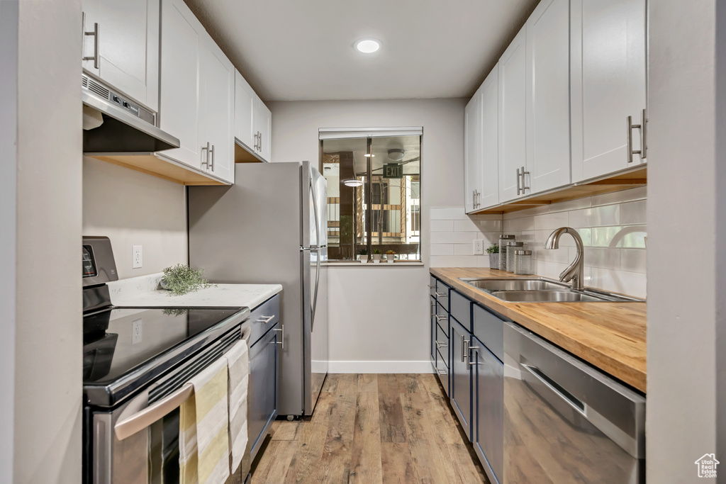 Kitchen featuring appliances with stainless steel finishes, under cabinet range hood, a sink, light wood-style flooring, and white cabinetry