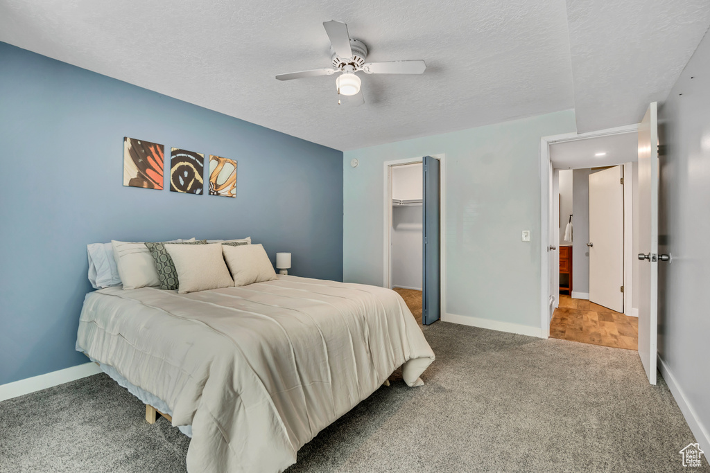 Carpeted bedroom with a textured ceiling, a closet, ceiling fan, baseboards, and a spacious closet