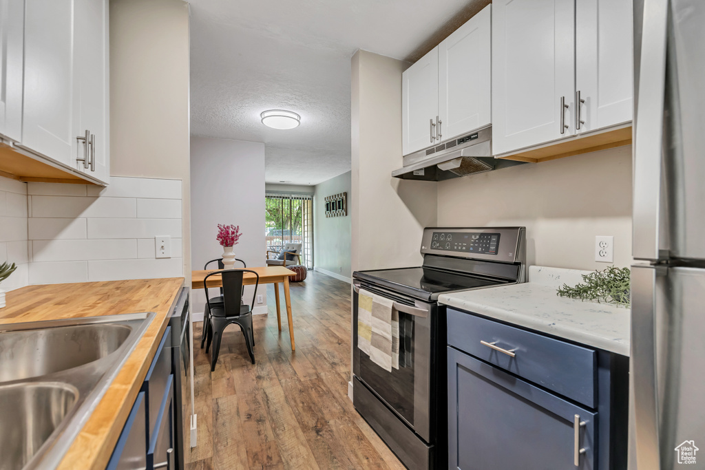 Kitchen with stainless steel appliances, under cabinet range hood, butcher block counters, hardwood / wood-style flooring, and white cabinets