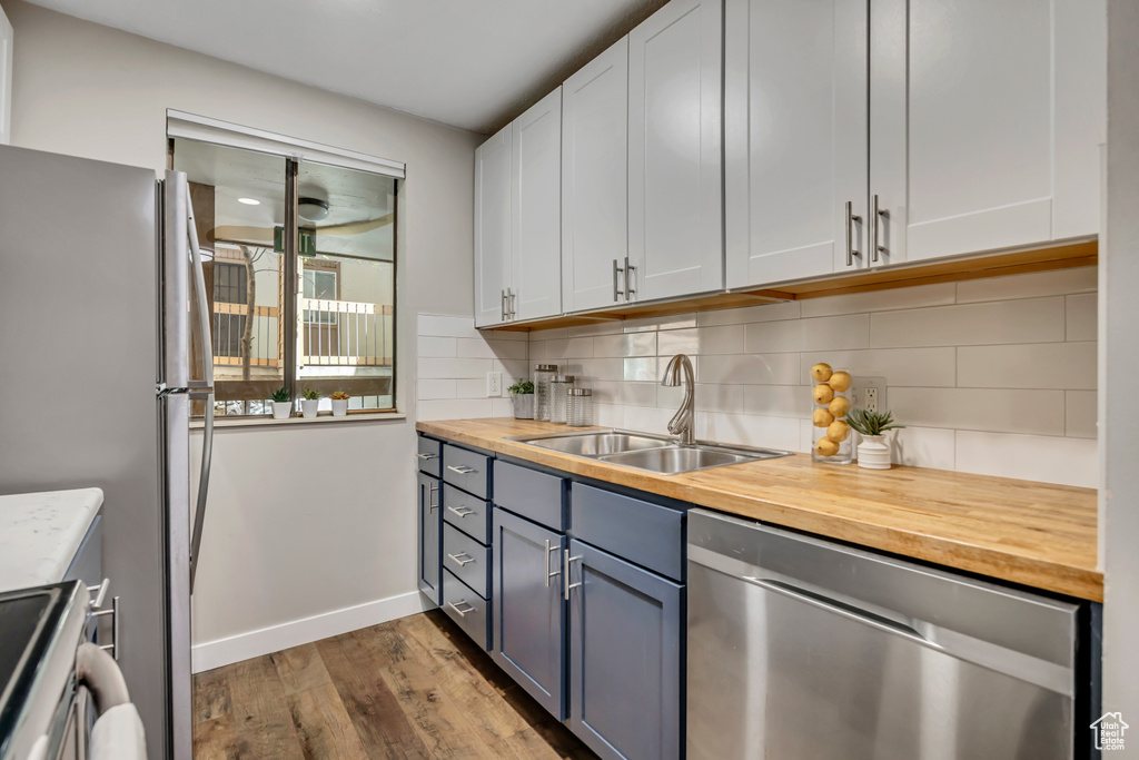Kitchen featuring stainless steel appliances, a sink, wood counters, dark wood finished floors, and tasteful backsplash