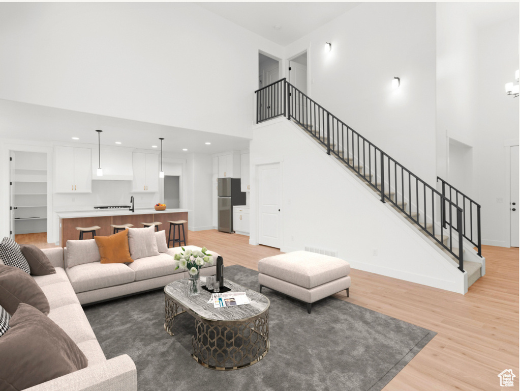 Living area featuring stairs, light wood-type flooring, baseboards, visible vents, and a high ceiling