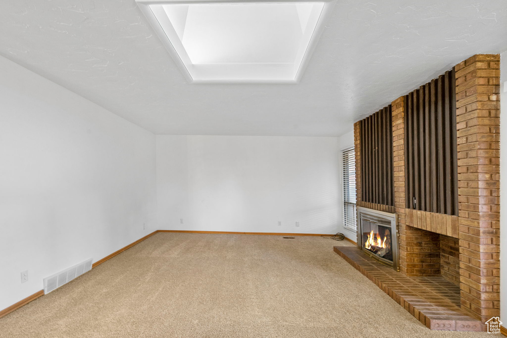 Unfurnished living room featuring a brick fireplace, visible vents, carpet flooring, and baseboards