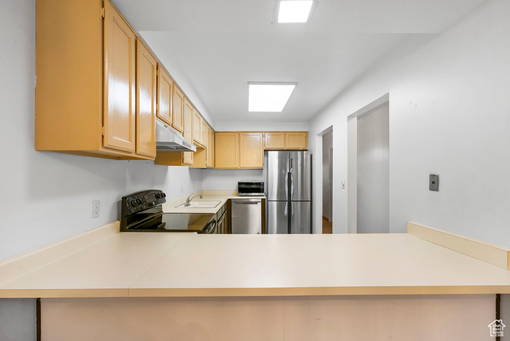 Kitchen featuring under cabinet range hood, appliances with stainless steel finishes, light countertops, a sink, and a peninsula
