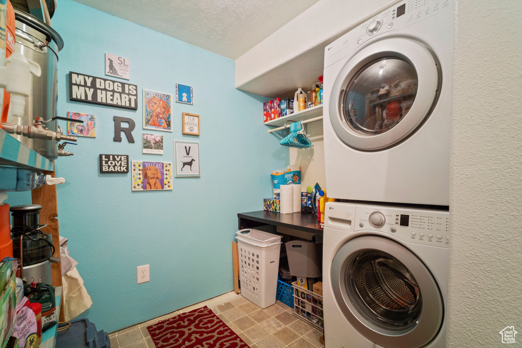 Washroom with a textured ceiling, stacked washer / drying machine, and laundry area