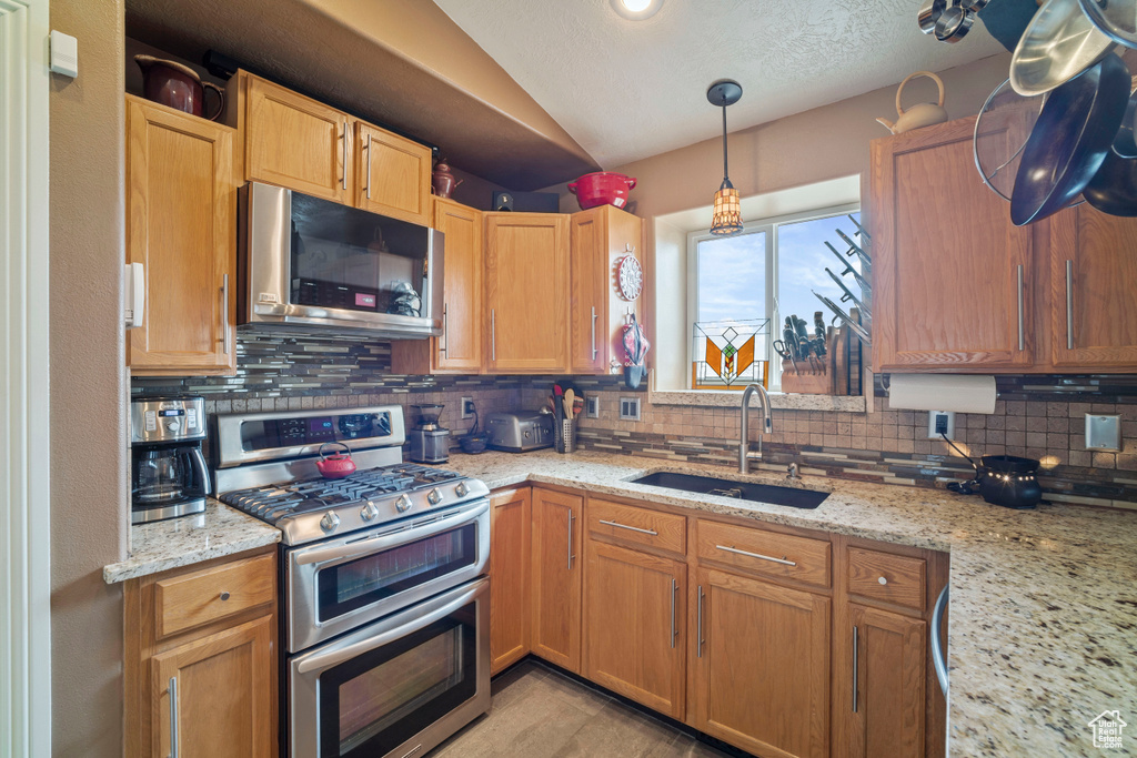 Kitchen featuring light stone countertops, stainless steel appliances, backsplash, a sink, and lofted ceiling