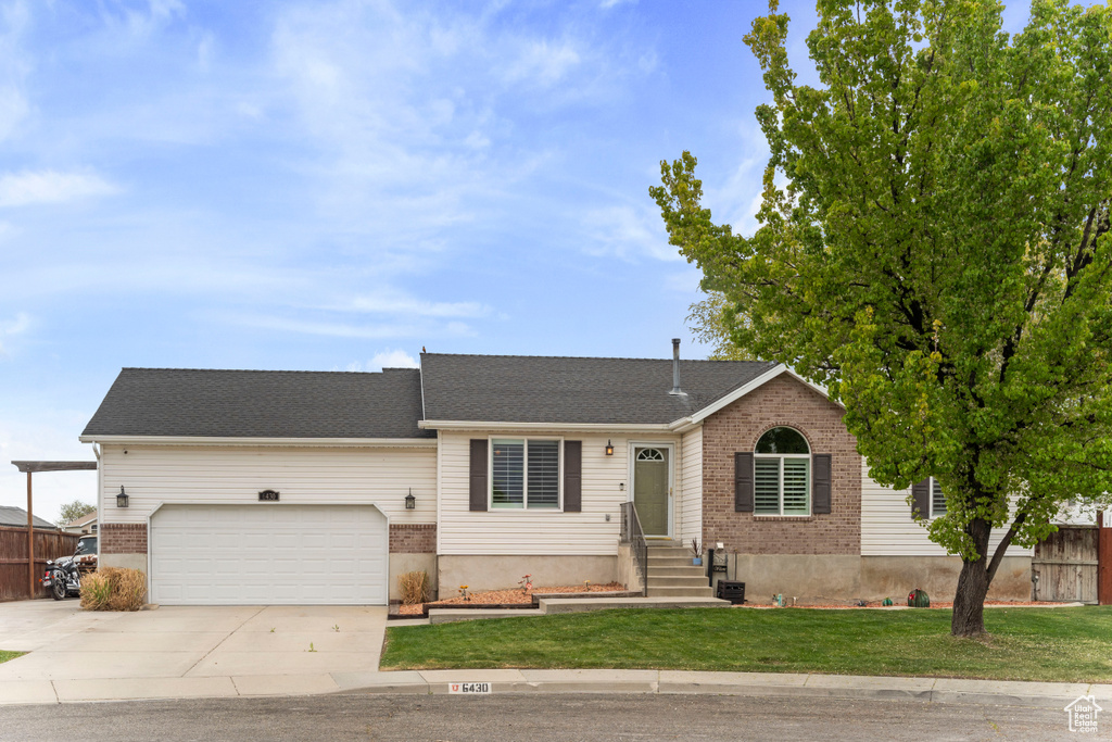 Ranch-style home with concrete driveway, an attached garage, fence, brick siding, and a front lawn