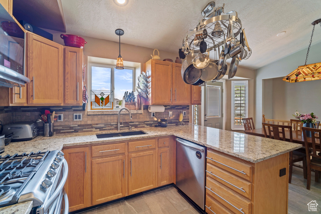 Kitchen featuring a textured ceiling, decorative backsplash, a sink, appliances with stainless steel finishes, and a peninsula