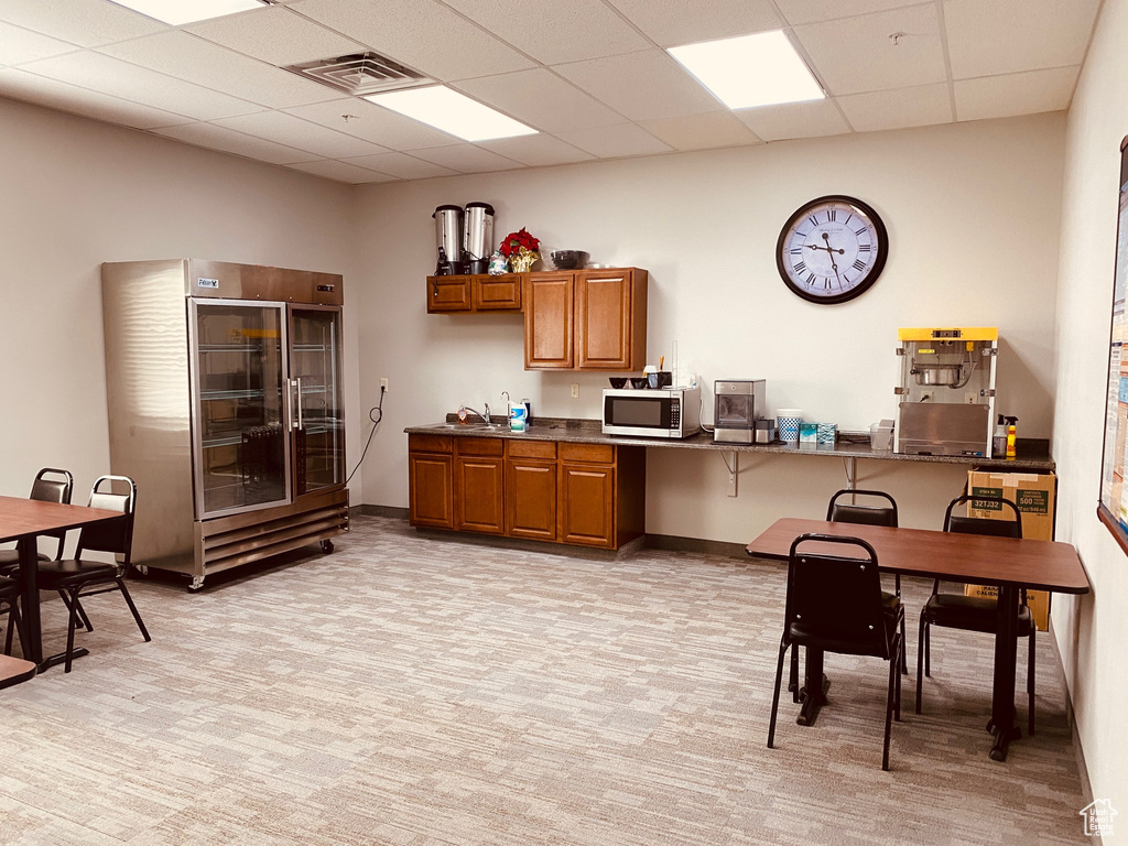 Kitchen with stainless steel microwave, brown cabinetry, light carpet, visible vents, and a paneled ceiling