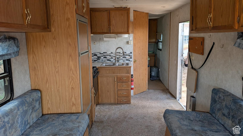 Kitchen with brown cabinets, light colored carpet, tasteful backsplash, and a sink