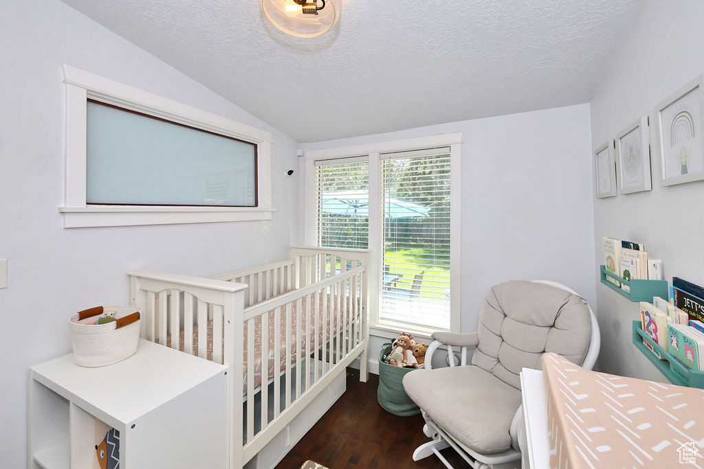 Bedroom featuring a textured ceiling, wood finished floors, lofted ceiling, and a crib