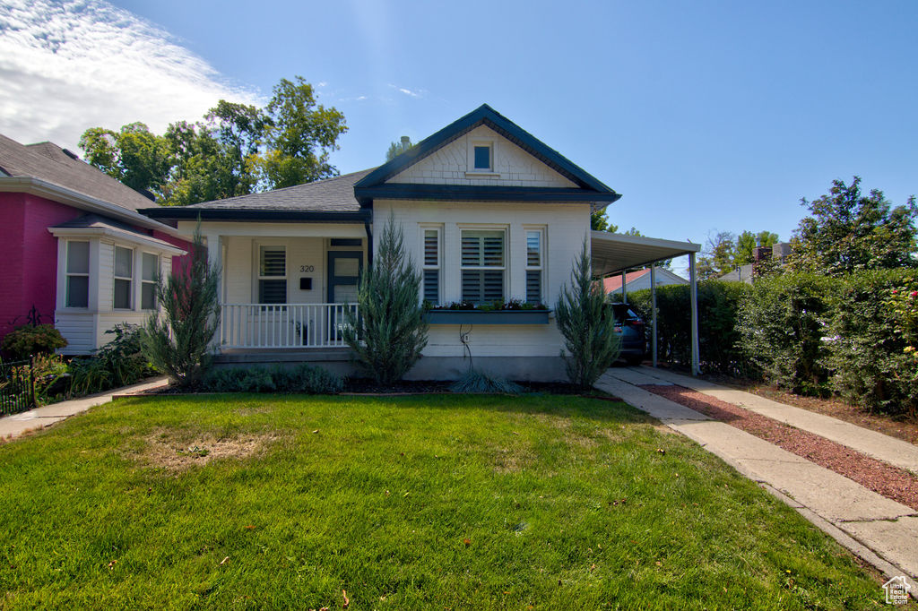 Bungalow-style house with an attached carport, a front yard, driveway, and covered porch