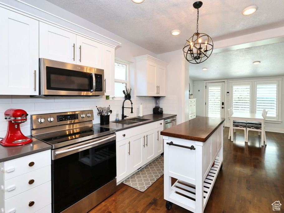 Kitchen featuring appliances with stainless steel finishes, a chandelier, white cabinets, dark wood finished floors, and a sink