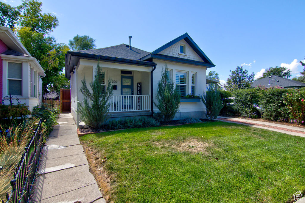 Bungalow featuring covered porch, a front yard, and fence