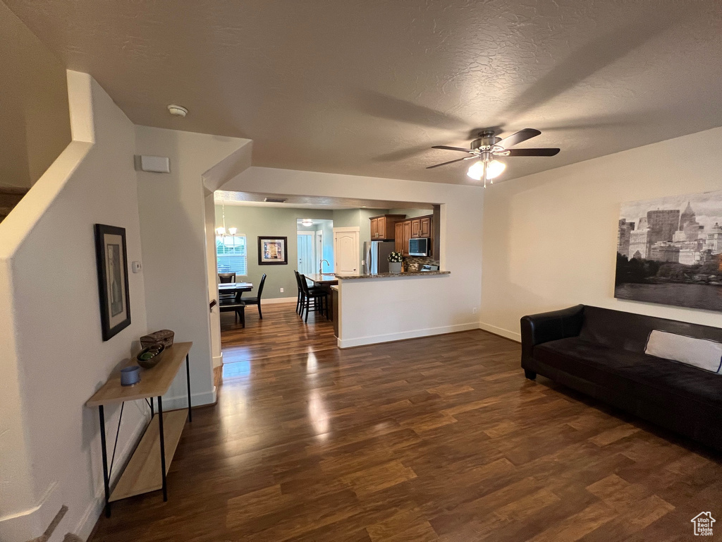 Living room featuring baseboards, ceiling fan with notable chandelier, dark wood-style flooring, and a textured ceiling